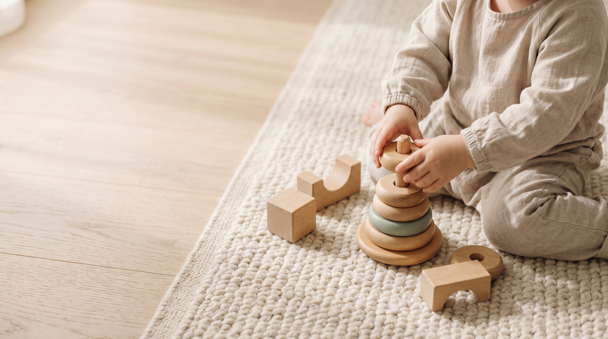 Toddler stacking a wooden ring stacker and blocks on a cream rug